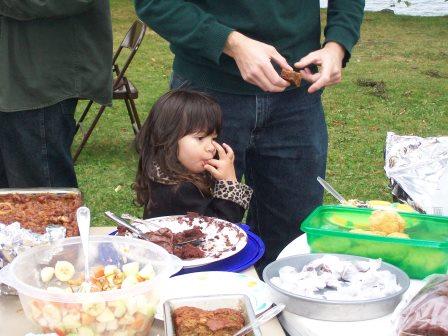 Child licking her fingers in front of a table of food at a picnic